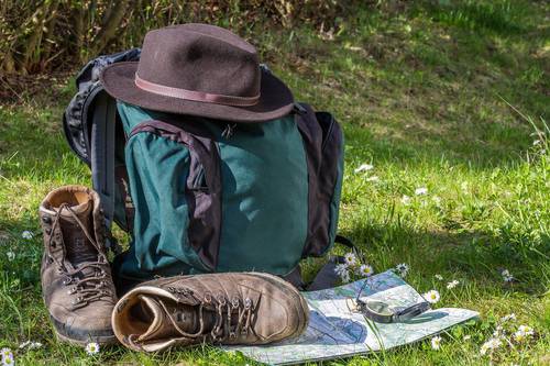 Stehender Wanderrucksack auf einer Wiese mit Wanderschuhen und Karte mit Kompass